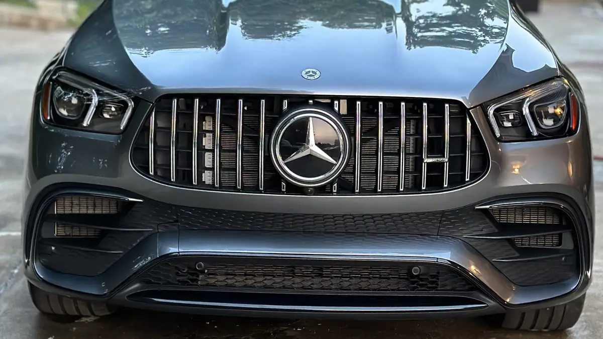 A dark grey Mercedes-AMG SUV photographed head-on, its glossy bodywork and chrome-slat grille reflecting an overcast sky.
