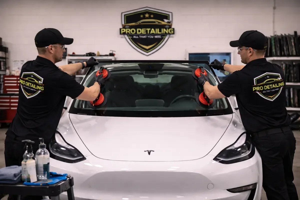 Two technicians working together across the windshield of a white electric sedan.
