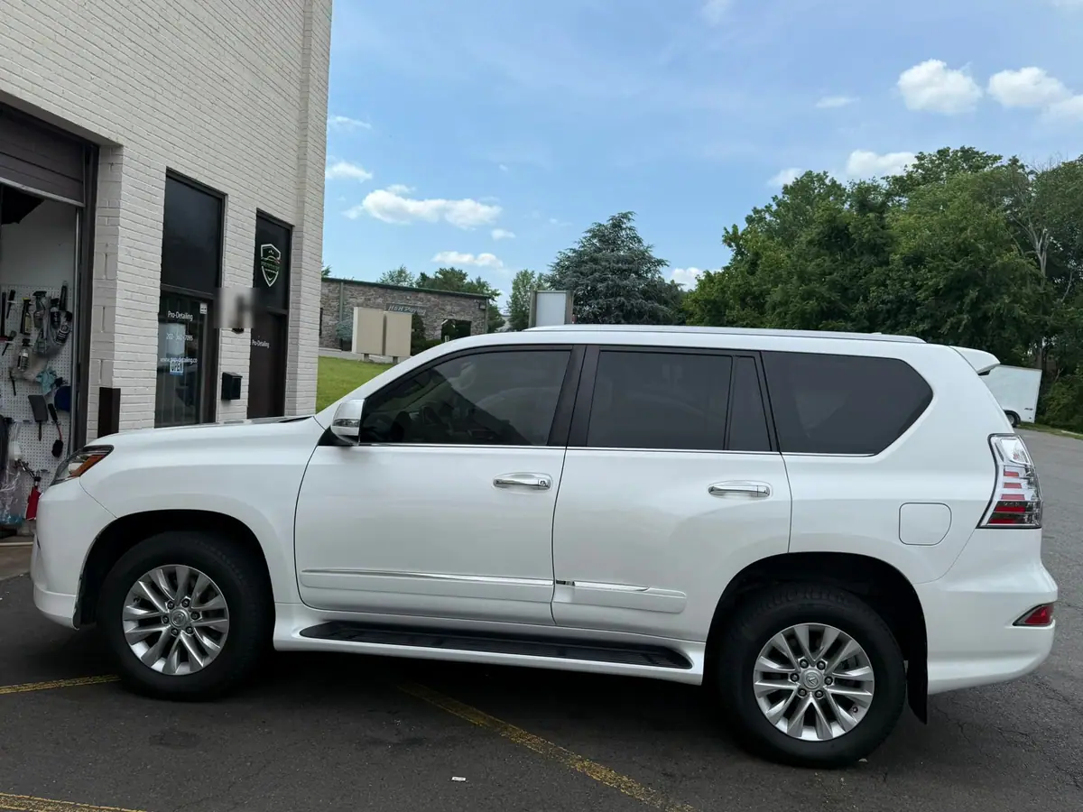 A white Lexus GX SUV parked in side profile on the asphalt outside PRO Detailing's white brick studio unit, with the roller shutter door open behind it on a bright summer day.