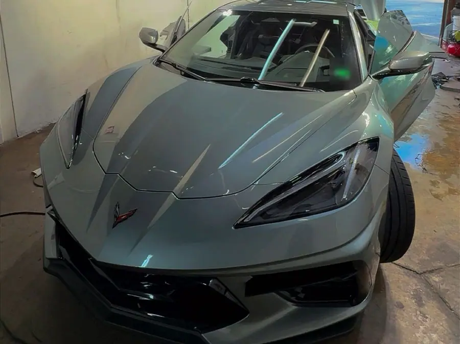 A light grey Chevrolet Corvette parked nose-first inside the workshop bay with its door and rear hatch raised.