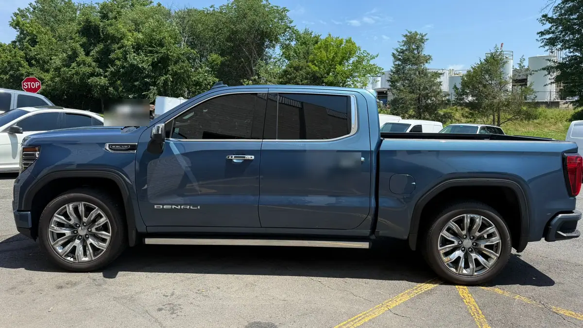 A metallic blue GMC Sierra Denali crew-cab pickup parked side-on in a sunlit lot.