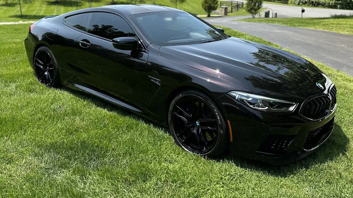 Gloss black BMW coupe reflecting a clear summer sky on a private driveway.