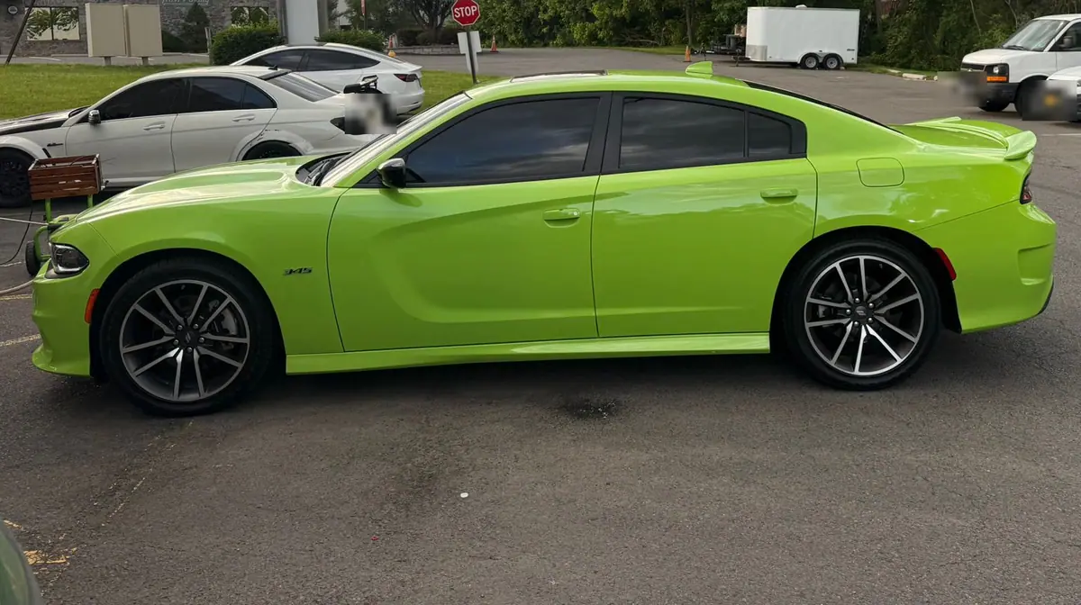 A bright lime green Dodge Charger parked side-on across an asphalt lot in evening light.