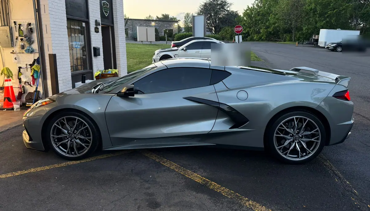 A silver-grey Chevrolet Corvette C8 parked in side profile outside the studio unit in low evening light.